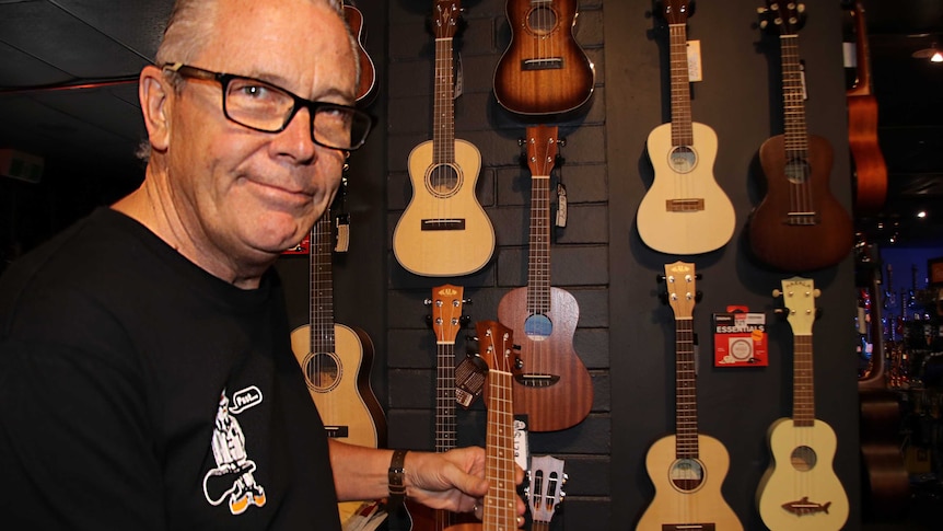 A man next to a range of ukuleles hanging on the wall of a music shop.