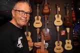 A man next to a range of ukuleles hanging on the wall of a music shop.