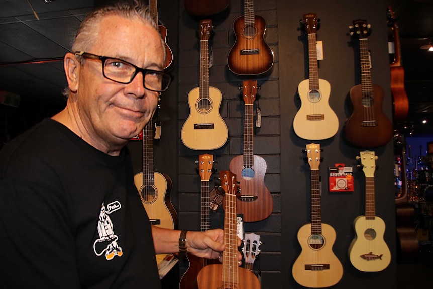 A man next to a range of ukuleles hanging on the wall of a music shop.