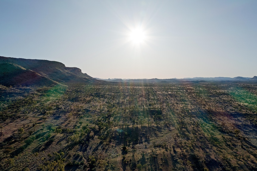 A sun starts to set over a vast plain, with ranges in the background. 