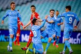 An A-League striker looks at his excited teammates who are congratulating him on his goal.