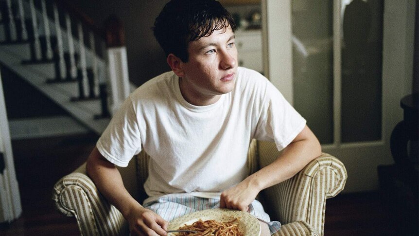 Barry Keoghan sitting in an armchair eating spaghetti in the 2017 film The Killing of a Sacred Deer.