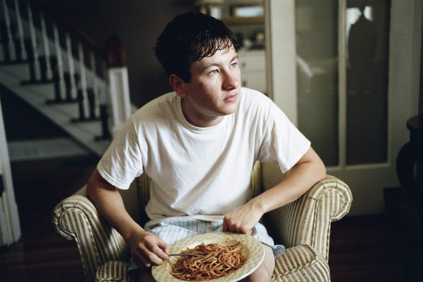 Barry Keoghan sitting in an armchair eating spaghetti in the 2017 film The Killing of a Sacred Deer.