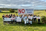 A group photo of people with matching shirts holding up signs opposing the abalone farm