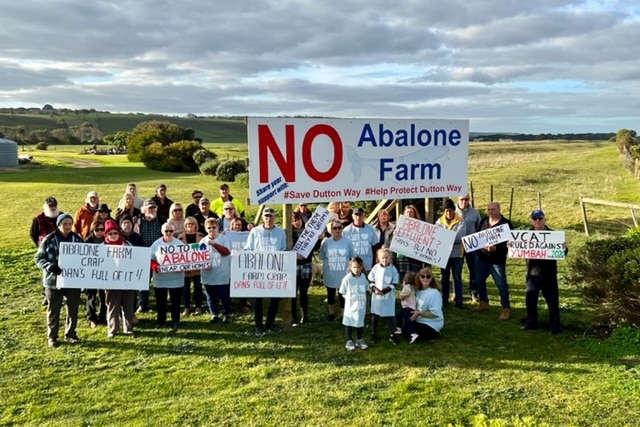 A group photo of people with matching shirts holding up signs opposing the abalone farm