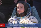 A woman wearing a white space suit and black headphones surrounded by people with bunch flowers in hand