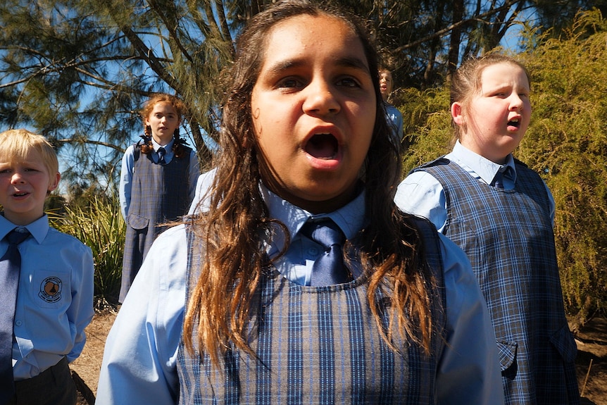 A group of school students in blue uniforms singing outside