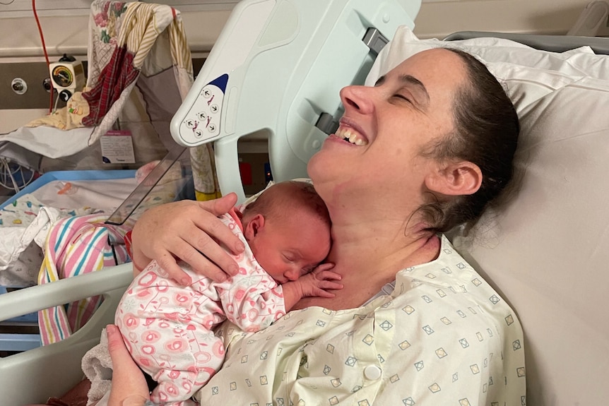 a woman in a hospital bed overcome with emotion as she holds her newborn