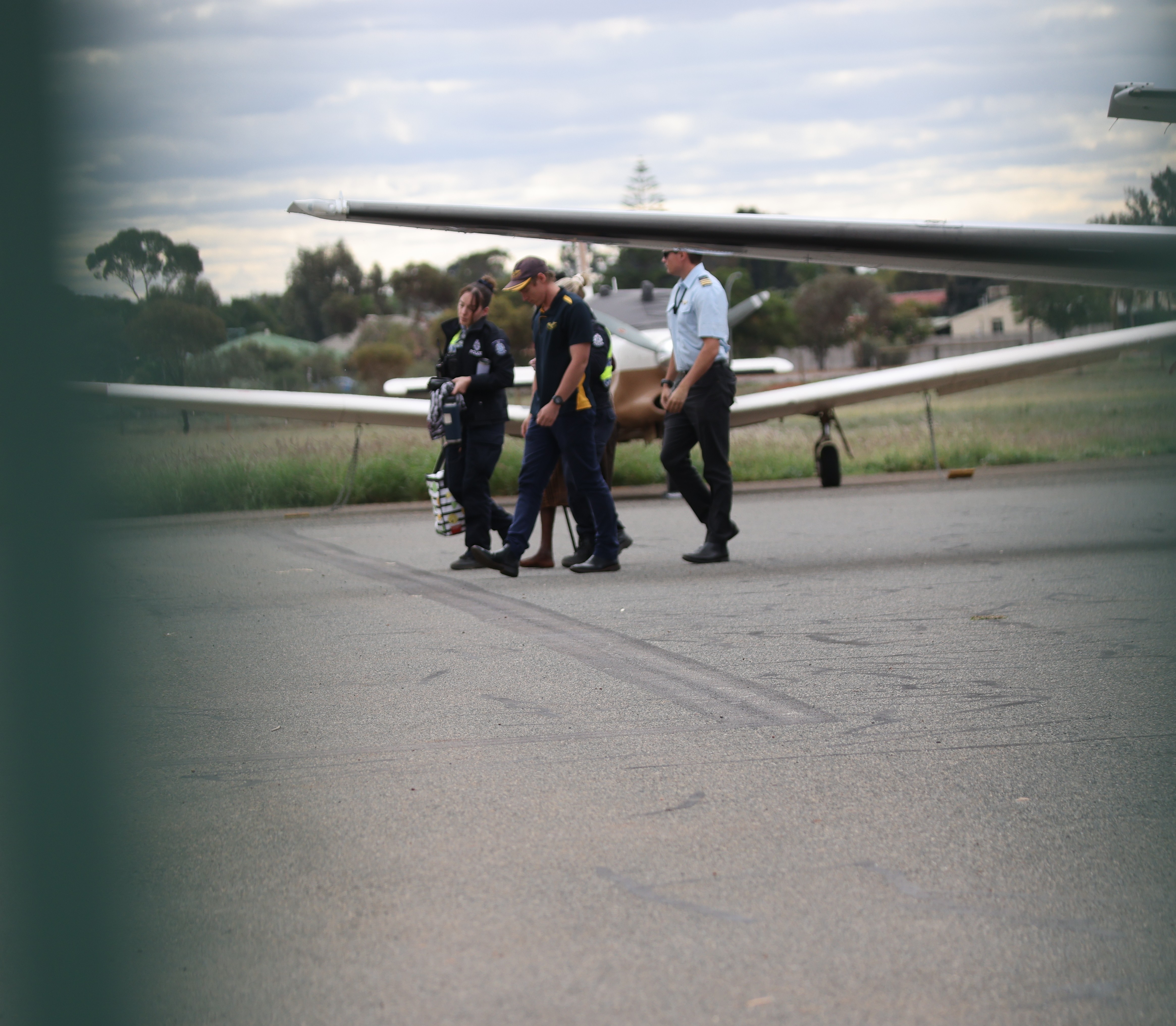 Four people walking in the distance with a plane wing in foreground