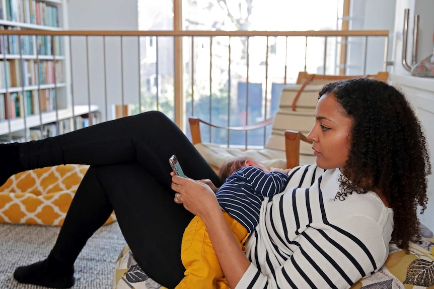 A woman nurses a baby while looking at a mobile phone.