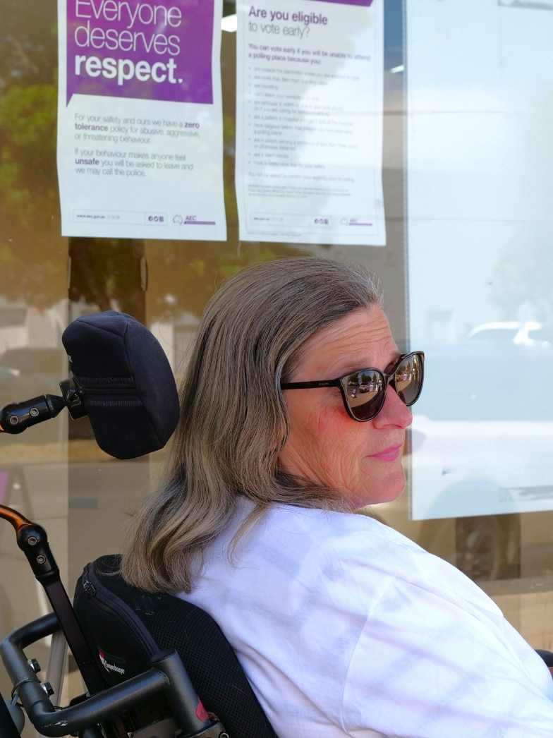 a woman wearing sunglasses and sitting in an electric wheelchair looking in the distance. 