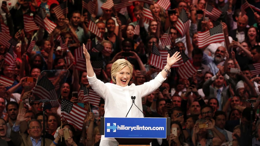 Hillary Clinton raises her arms and looks at a crowd.