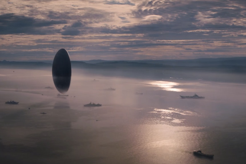 A screen shot from film. A UFO hovers over the water surrounded by battle ships.