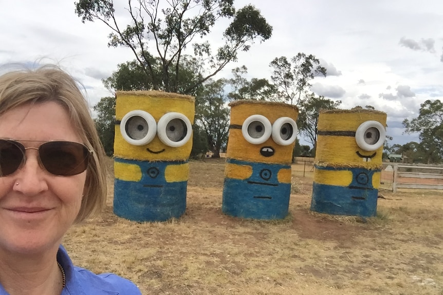 A selfie photo of reporter Lisa Herbert, standing in front of blue and yellow painted hay bales that look like minions