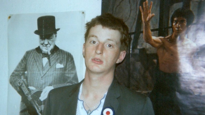 A young Billy Bragg, in a suit coat, stares at the camera