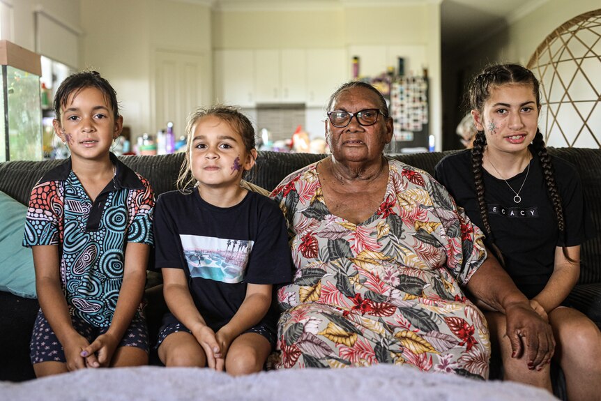 An Indigenous elder sits on a couch with her three great granddaughters.