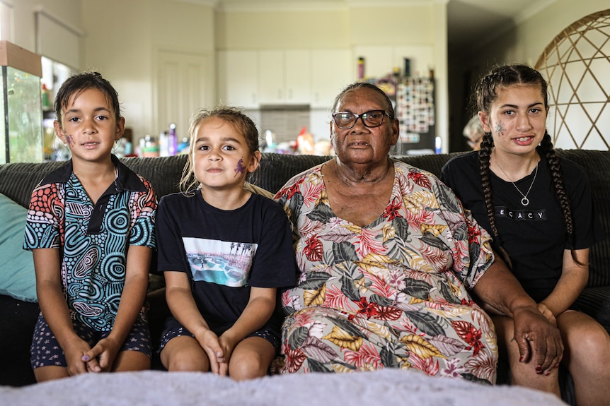 An Indigenous elder sits on a couch with her three great granddaughters.
