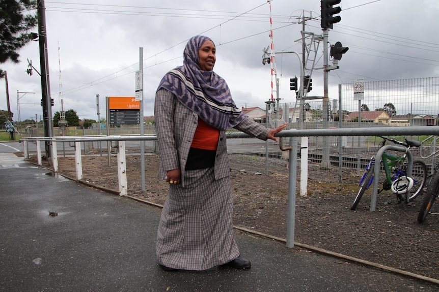 Anaab Rooble holds a railing as she walks towards a train station with the railway behind her