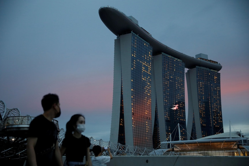 Two masked people in the foreground, with huge, three-pronged building of Singapore's Marina Bay Sands hotel in the background. 
