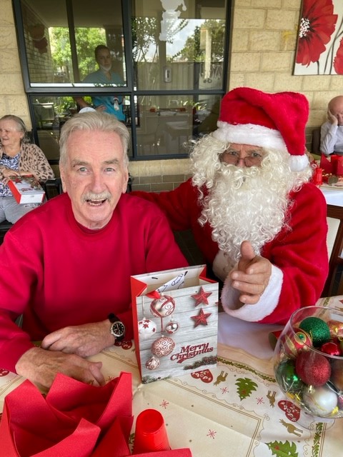 An elderly man in a red sweatshirt seated next to a man dressed as Santa.