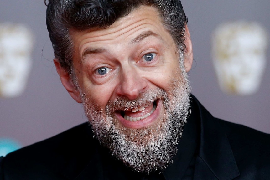 A tight close up of Andy Serkis's bearded face smiling widely.