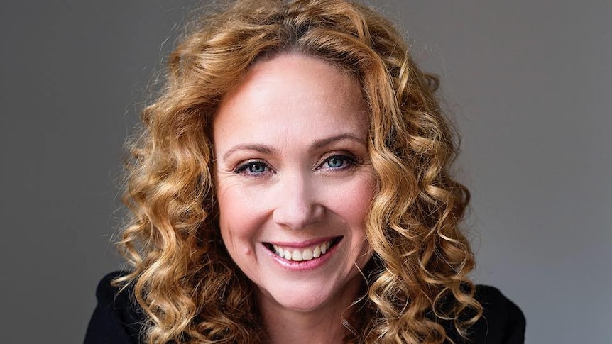 A portrait shot of Ms Horne, who is smiling and has curly reddish hair hanging past her shoulder. Her arms are crossed.