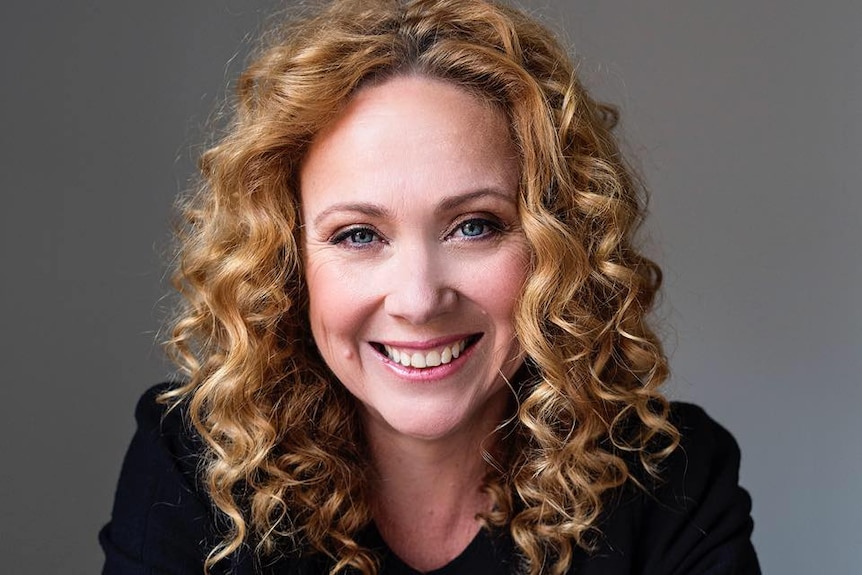 A portrait shot of Ms Horne, who is smiling and has curly reddish hair hanging past her shoulder. Her arms are crossed.