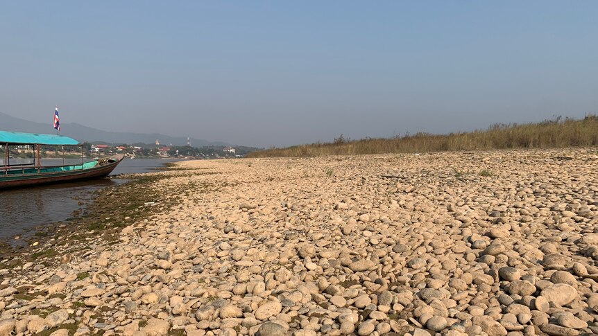 A boat sits on the rocky banks of a very depleted Mekong River.