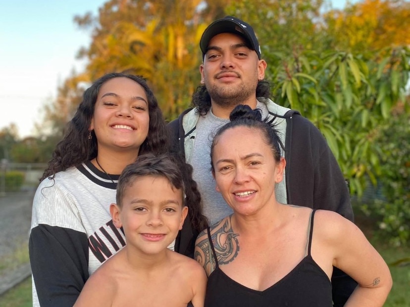 Moana smiling in a photo with her two sons and daughter, outdoors in a leafy area.