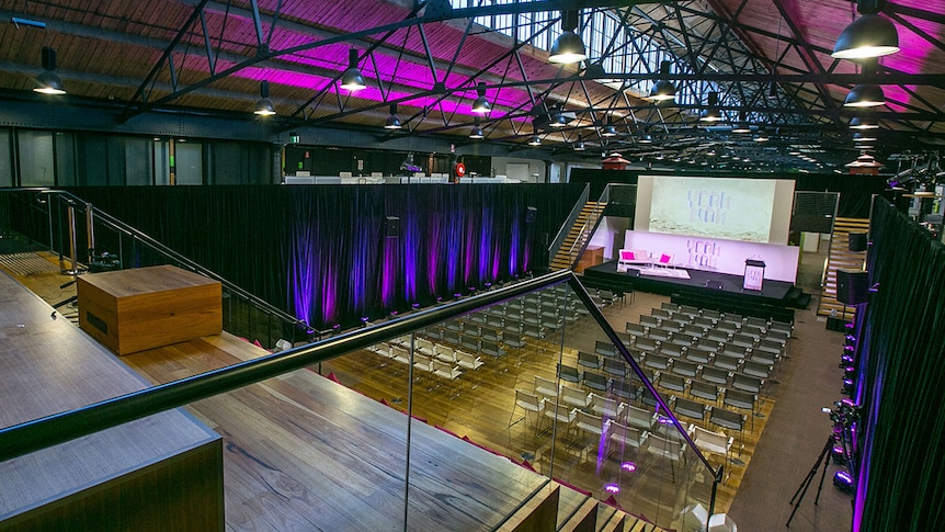 A large auditorium with black rafter beams and timber stadium seating.