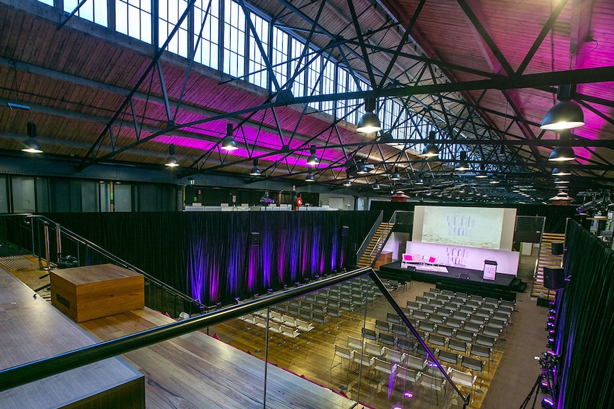 A large auditorium with black rafter beams and timber stadium seating.