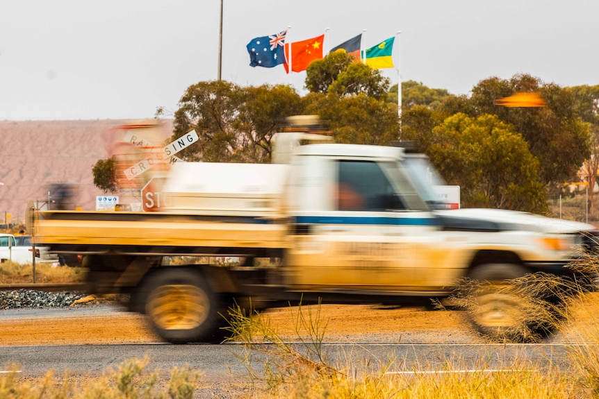 A blurry four-wheel-drive vehicle flashes past on the highway in front of the entrance to a gold mine 