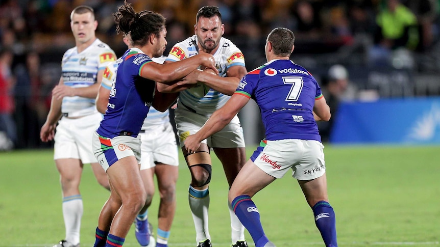 Ryan James stands upright holding the ball as he is tackled by the Warriors defence.