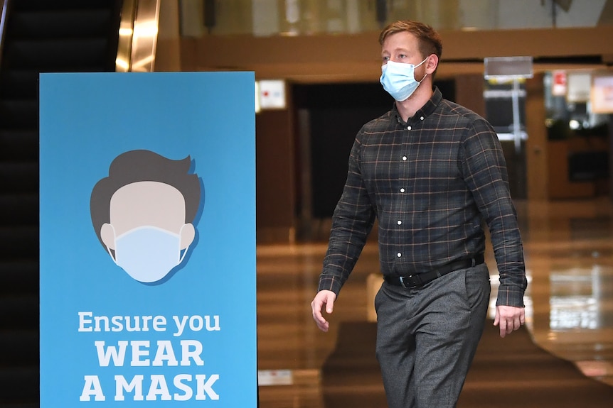 A man wearing a face mask walks past a sign advising people to wear face masks in Brisbane