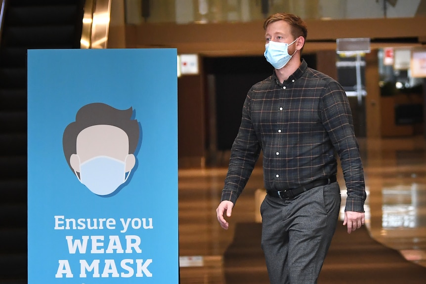 Un hombre que llevaba una máscara facial pasa junto a un cartel que aconseja a las personas que usen máscaras faciales en Brisbane
