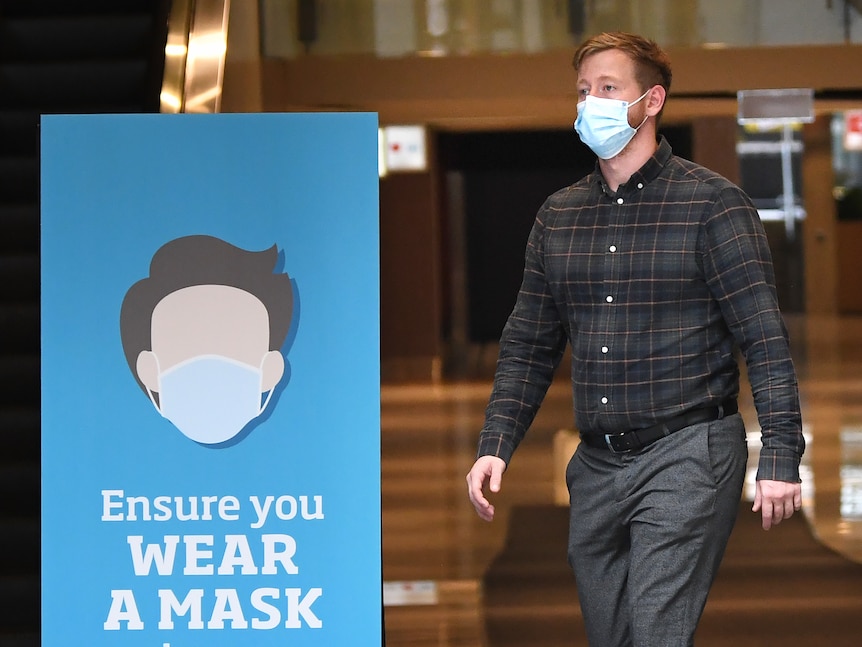 A man wearing a face mask walks past a sign advising people to wear face masks in Brisbane