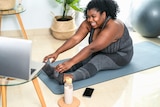 A young woman does a virtual fitness class on a yoga mat.