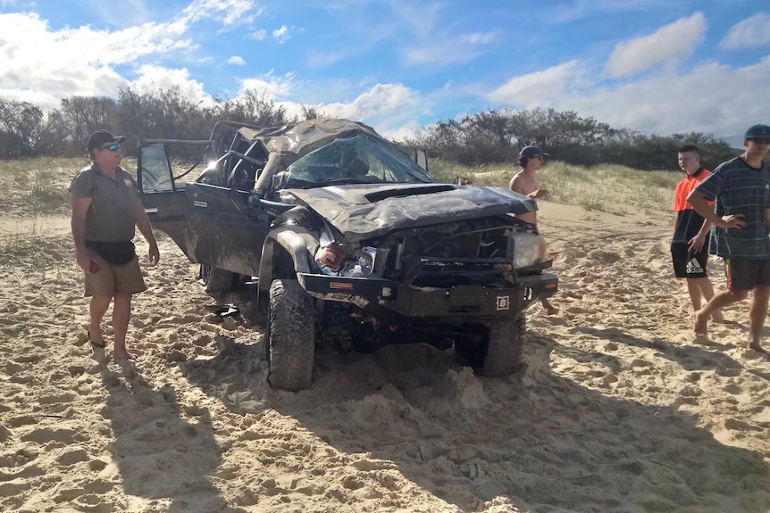 Five men stand near a damaged black four wheel drive