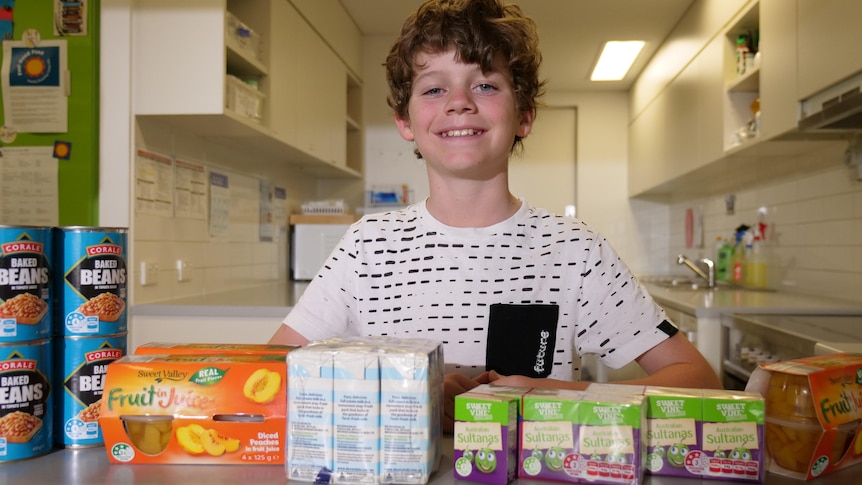a 10-year-old boy smiles surrounded by non-perishable foods.