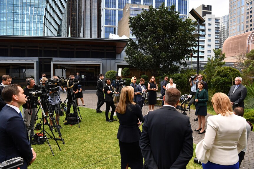 The Premier stands at the front of a media pack.