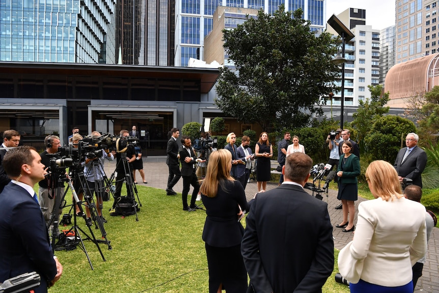 The Premier stands at the front of a media pack.