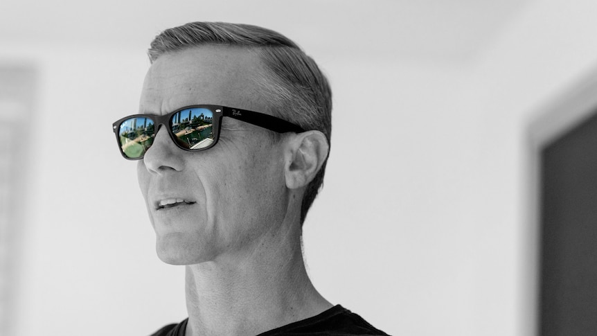 A portrait of Troy Hunt in greyscale with only the Gold Coast skyline reflection in his sunglasses in colour
