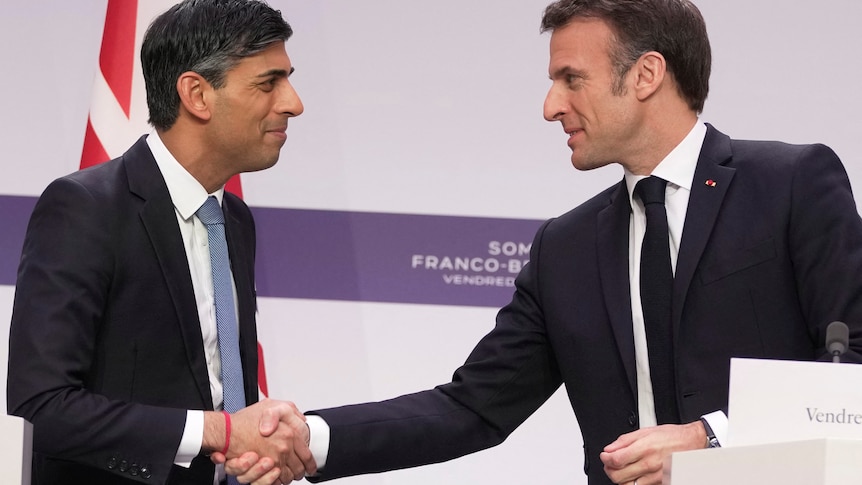 The two men shake hands on a stage bearing logos of the Franco-British summit