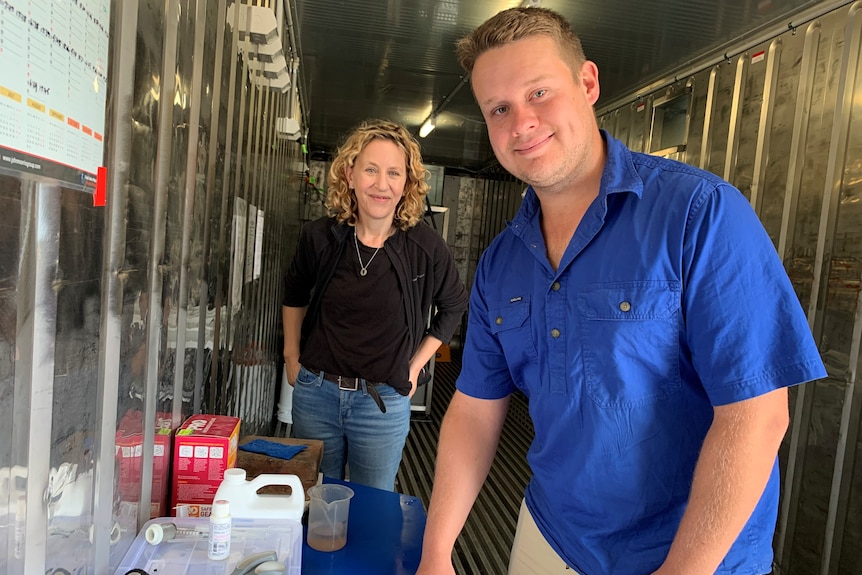 Dr Amina Price and Zac Rolfe stand at the front of a shipping container with fish tanks behind them