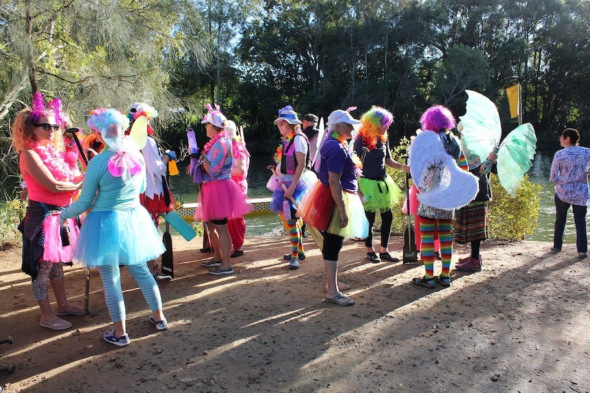 Women in extremely colourful outfits and fairy wings stand on a bank
