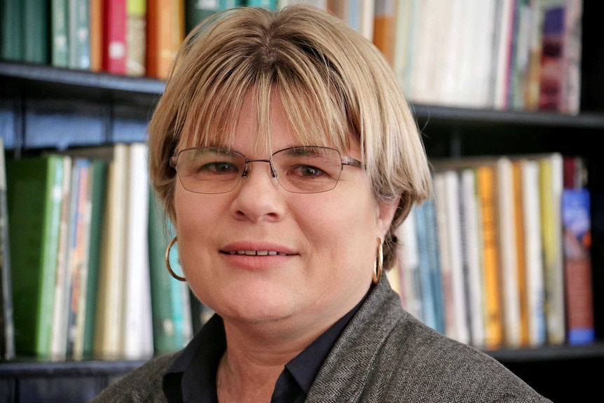 Headshot of a woman wearing glasses with a bookshelf in the background.