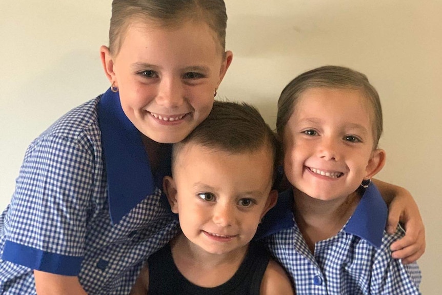 Three children hug and smile.