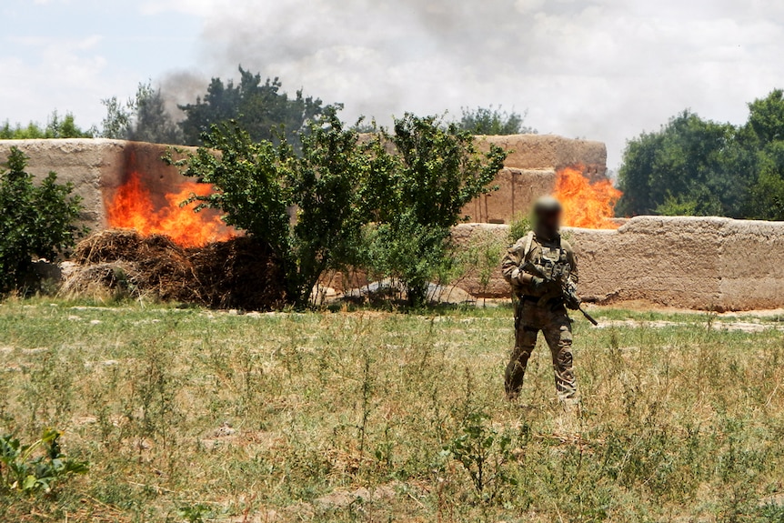 SAS soldier patrols in front of burning building in Afghanistan in 2012.