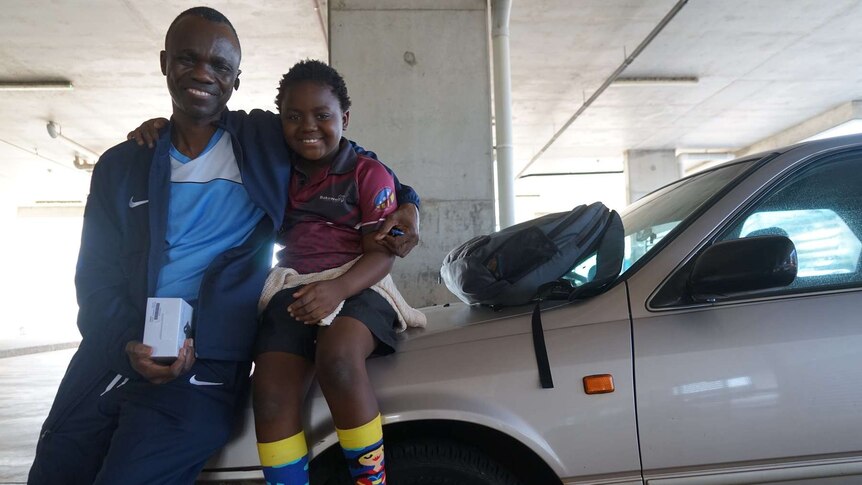 Renter Patrick Mossongo and his son sit on a car bonnet.