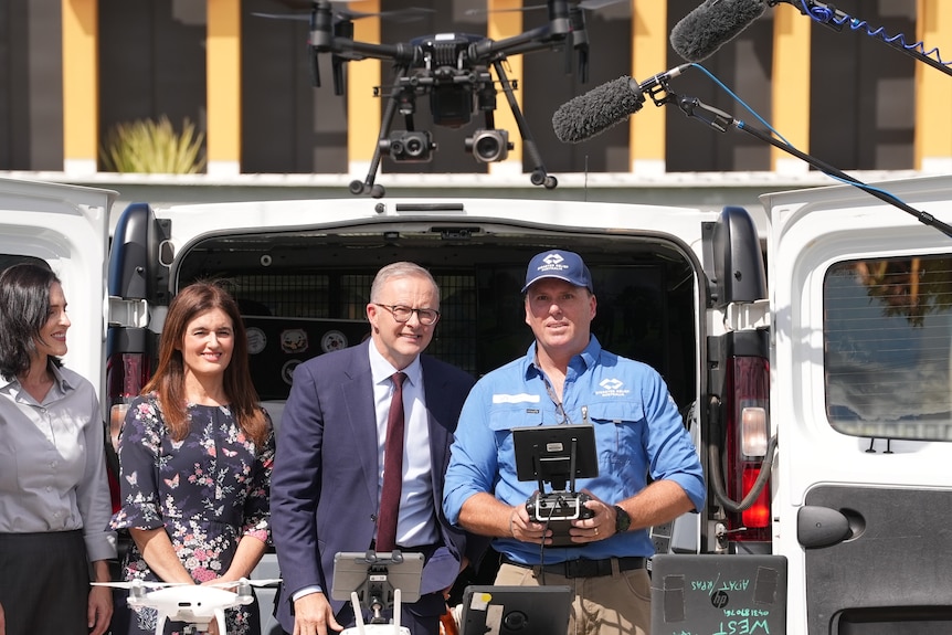 Anthony Albanese stands next to a man while a drone flies above his head. 